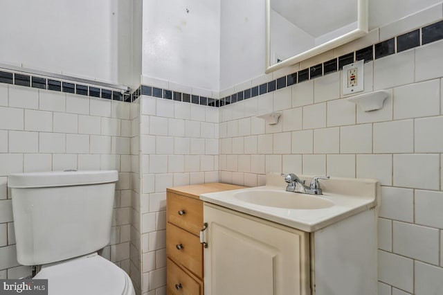 bathroom with toilet, tasteful backsplash, vanity, and tile walls