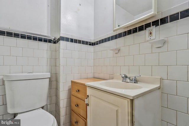 bathroom featuring toilet, vanity, and tile walls