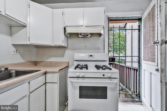 kitchen featuring white cabinets, under cabinet range hood, light countertops, a sink, and white gas stove
