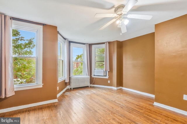 unfurnished room featuring radiator, hardwood / wood-style floors, a healthy amount of sunlight, and baseboards