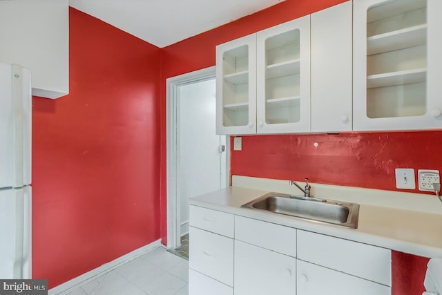 kitchen with light tile patterned flooring, white cabinets, white fridge, and sink