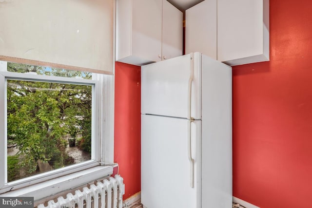 kitchen with white fridge, radiator, a wealth of natural light, and white cabinets