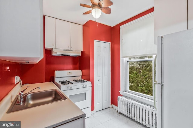 kitchen with white appliances, sink, radiator heating unit, ceiling fan, and white cabinets