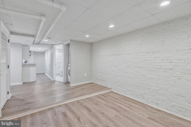 finished basement with washer / dryer, light wood-style floors, baseboards, and brick wall