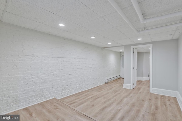 basement with light hardwood / wood-style floors, a paneled ceiling, and baseboard heating