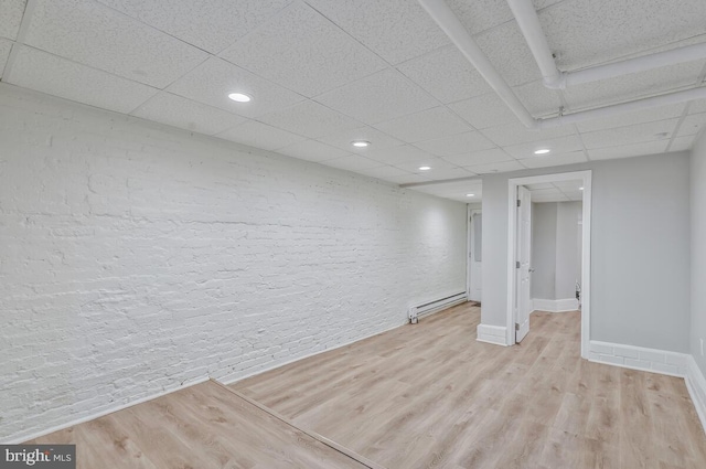 finished below grade area featuring baseboard heating, light wood-style floors, a paneled ceiling, and recessed lighting