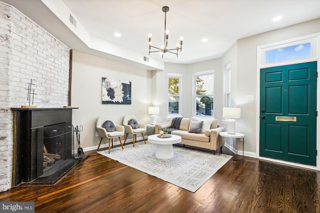 living room with a notable chandelier, a brick fireplace, and dark hardwood / wood-style floors