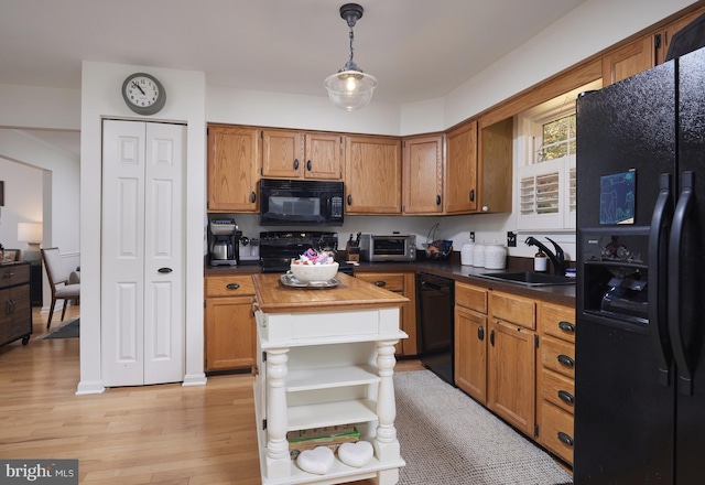 kitchen with sink, black appliances, decorative light fixtures, and light hardwood / wood-style flooring