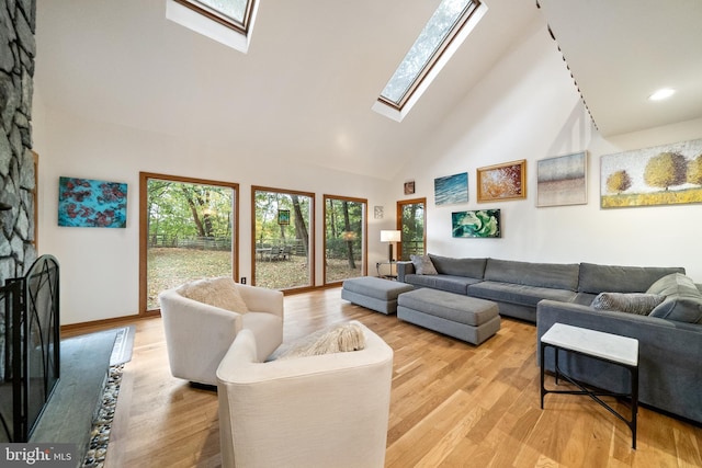 living room featuring light hardwood / wood-style floors, high vaulted ceiling, and a skylight