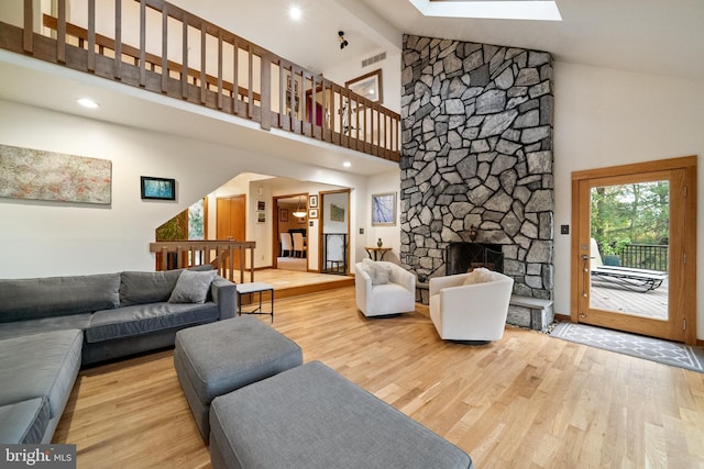 living room with beamed ceiling, light hardwood / wood-style flooring, a fireplace, high vaulted ceiling, and a skylight