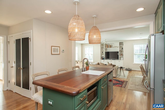 kitchen featuring an island with sink, light wood-type flooring, stainless steel appliances, sink, and green cabinetry