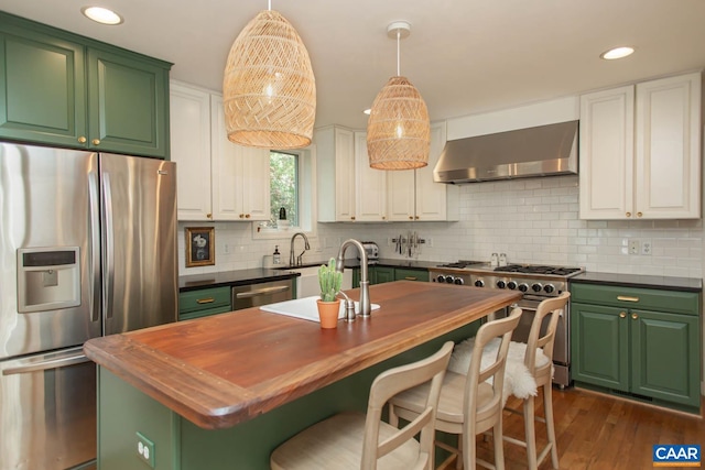 kitchen with wall chimney range hood, white cabinets, tasteful backsplash, an island with sink, and stainless steel appliances