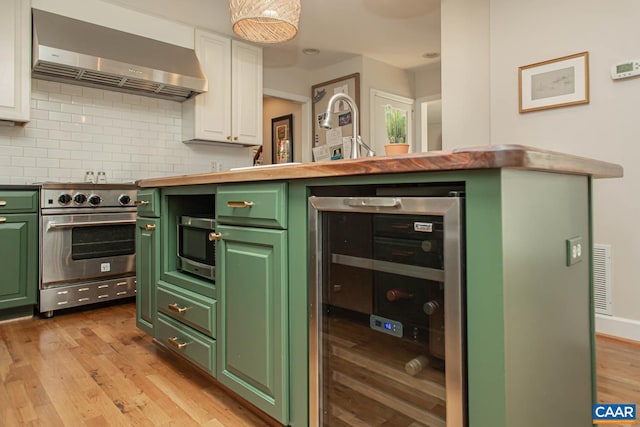 kitchen featuring white cabinets, appliances with stainless steel finishes, light hardwood / wood-style floors, beverage cooler, and extractor fan