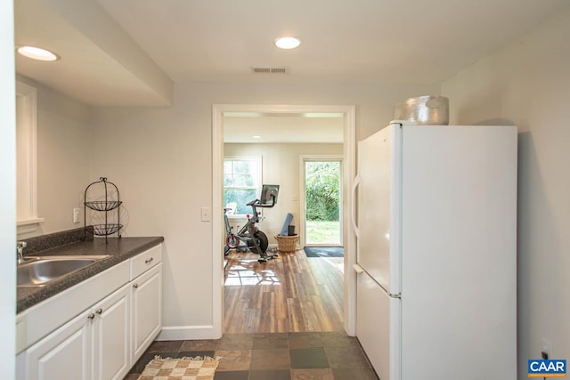 kitchen featuring white fridge, dark wood-type flooring, sink, and white cabinets