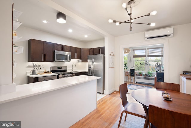 kitchen with radiator, light wood-type flooring, a wall mounted air conditioner, pendant lighting, and stainless steel appliances