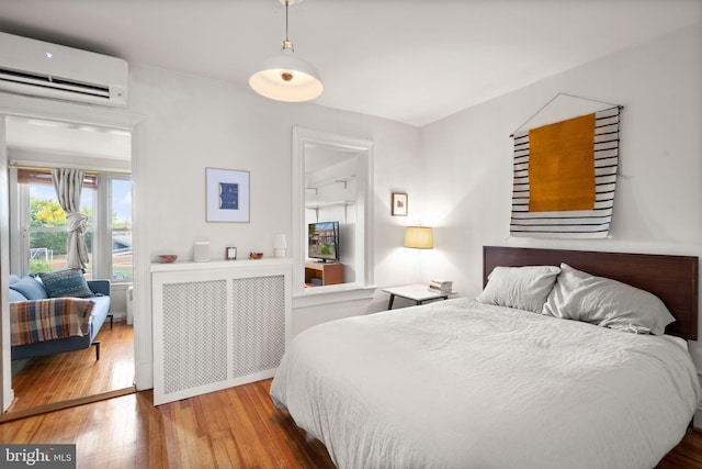 bedroom featuring a wall unit AC, hardwood / wood-style floors, and radiator heating unit