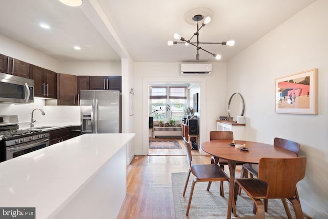 kitchen with light hardwood / wood-style flooring, a wall mounted air conditioner, sink, decorative light fixtures, and appliances with stainless steel finishes