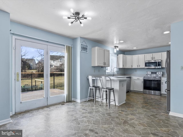 kitchen with appliances with stainless steel finishes, a breakfast bar, white cabinets, kitchen peninsula, and a textured ceiling