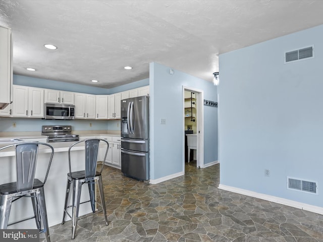 kitchen with stainless steel appliances, a breakfast bar, white cabinets, and a textured ceiling