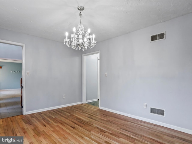 spare room with hardwood / wood-style flooring and a chandelier