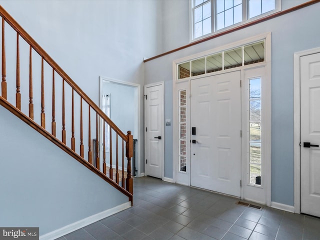 entrance foyer featuring dark tile patterned flooring, a towering ceiling, and a wealth of natural light