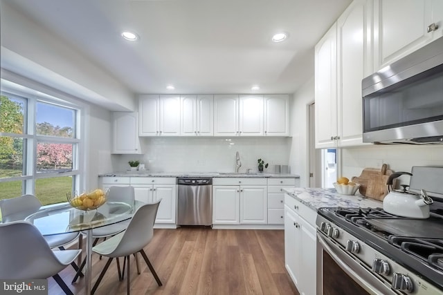 kitchen with appliances with stainless steel finishes, white cabinetry, hardwood / wood-style flooring, light stone countertops, and sink