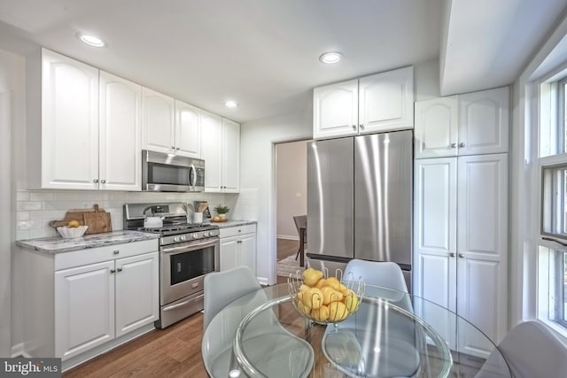 kitchen featuring decorative backsplash, dark hardwood / wood-style floors, white cabinetry, appliances with stainless steel finishes, and light stone counters