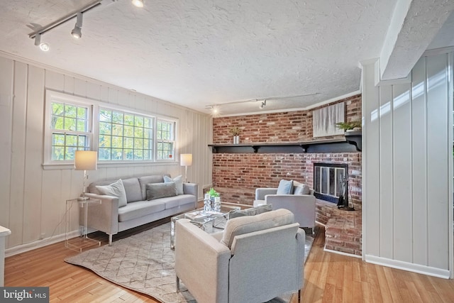 living room with brick wall, track lighting, light hardwood / wood-style flooring, and a brick fireplace