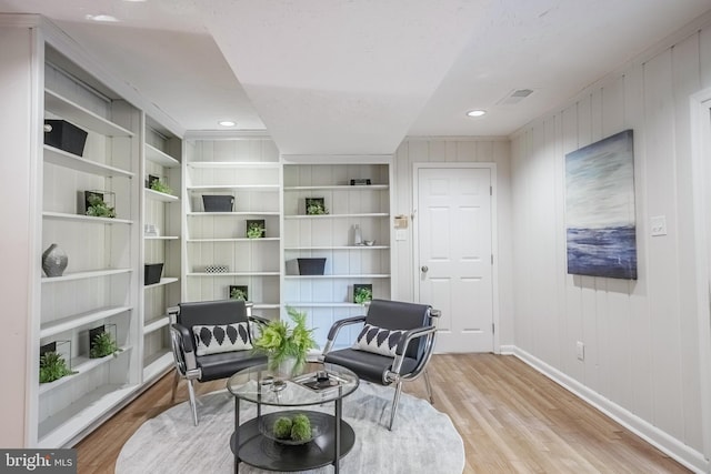 sitting room featuring light hardwood / wood-style flooring, wood walls, and built in features