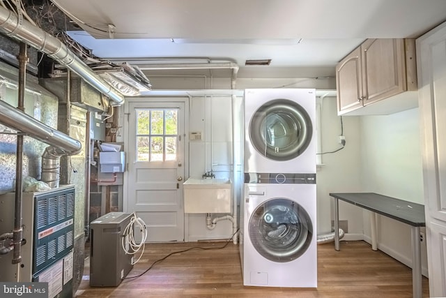 laundry room featuring sink, dark wood-type flooring, stacked washer and clothes dryer, and cabinets