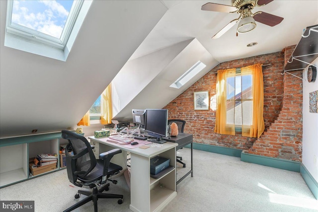 carpeted office featuring vaulted ceiling with skylight, ceiling fan, and brick wall