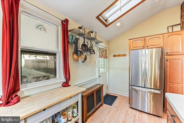 kitchen with stainless steel refrigerator, a healthy amount of sunlight, light wood-type flooring, and lofted ceiling with skylight