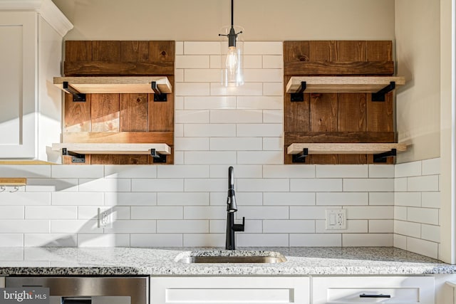 kitchen featuring tasteful backsplash, light stone countertops, sink, pendant lighting, and white cabinets