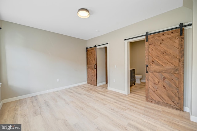 unfurnished bedroom with ensuite bathroom, light hardwood / wood-style flooring, and a barn door