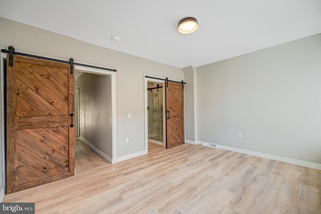 unfurnished bedroom featuring light hardwood / wood-style floors, a barn door, and ensuite bath