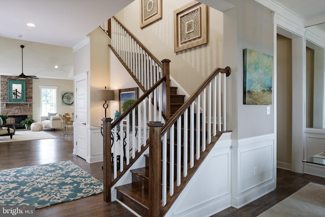 staircase featuring ornamental molding, hardwood / wood-style floors, and a stone fireplace