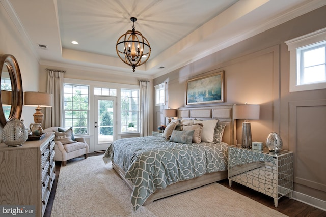 bedroom with a tray ceiling, dark wood-type flooring, multiple windows, and access to outside