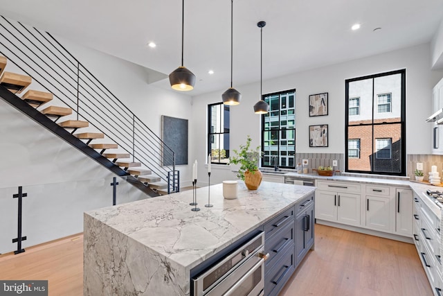 kitchen featuring hanging light fixtures, backsplash, light stone countertops, a center island, and white cabinetry