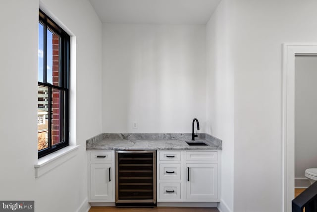 bar with beverage cooler, light stone countertops, sink, white cabinets, and hardwood / wood-style flooring