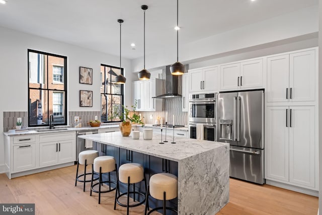 kitchen featuring wall chimney range hood, appliances with stainless steel finishes, a kitchen island, pendant lighting, and decorative backsplash