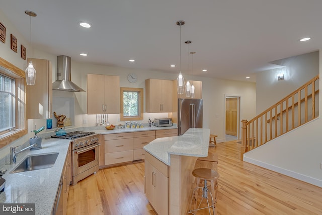 kitchen featuring light brown cabinetry, premium appliances, wall chimney range hood, and light hardwood / wood-style flooring