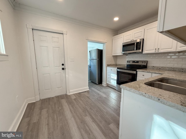 kitchen featuring ornamental molding, white cabinetry, stainless steel appliances, and light hardwood / wood-style flooring