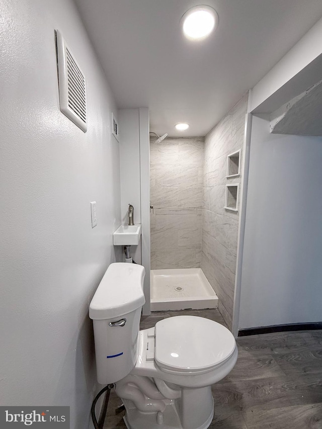 bathroom with tiled shower, hardwood / wood-style floors, and toilet