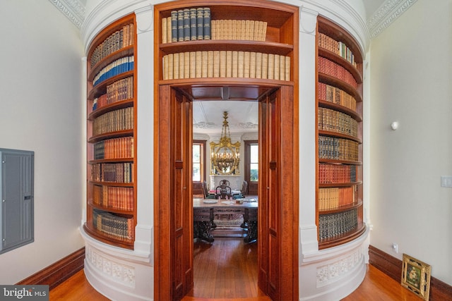 corridor featuring ornamental molding, hardwood / wood-style flooring, and an inviting chandelier