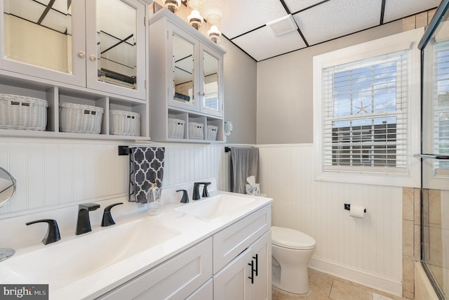 bathroom featuring toilet, a paneled ceiling, tile patterned floors, walk in shower, and vanity