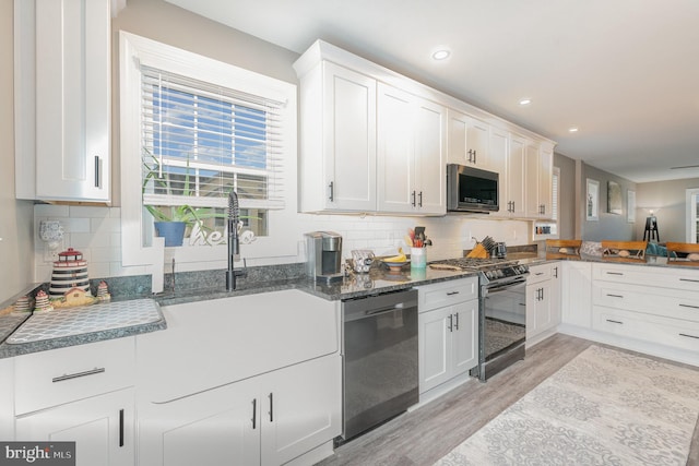 kitchen with appliances with stainless steel finishes, backsplash, light hardwood / wood-style floors, dark stone counters, and white cabinets