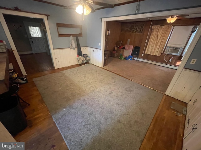 basement with dark wood-type flooring, ceiling fan, a baseboard heating unit, and wooden walls