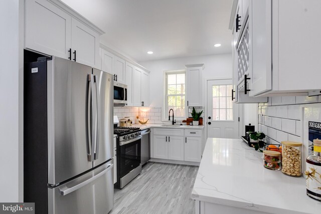 kitchen with light stone countertops, appliances with stainless steel finishes, sink, light wood-type flooring, and white cabinetry