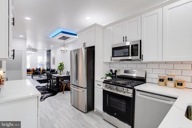 kitchen featuring white cabinets, tasteful backsplash, appliances with stainless steel finishes, light wood-type flooring, and pendant lighting