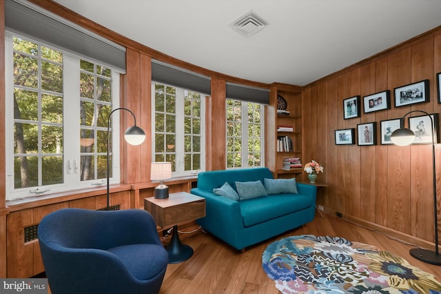 sitting room with a healthy amount of sunlight, wooden walls, light wood-type flooring, and built in shelves